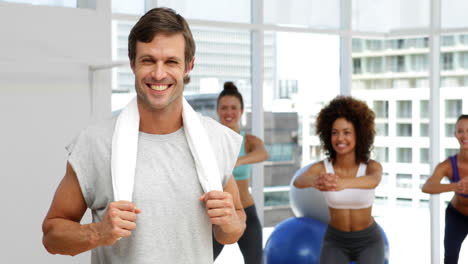 Fitness-class-squatting-on-bosu-balls-while-instructor-smiles-at-camera