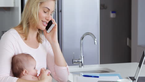 Madre-Haciendo-Una-Llamada-Telefónica-Y-Sosteniendo-A-Un-Bebé