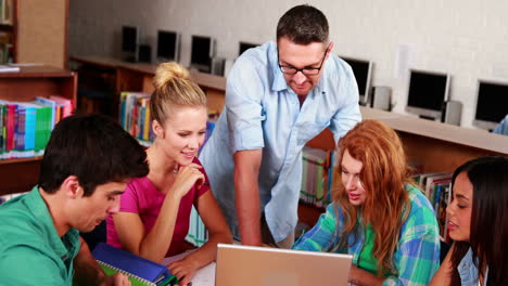 Glückliche-Schüler,-Die-Gemeinsam-Mit-Ihrem-Tutor-In-Der-Bibliothek-Arbeiten