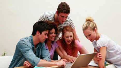 Cheerful-students-using-laptop-together