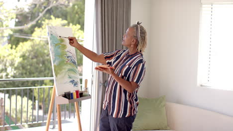 A-senior-African-American-woman-with-grey-braided-hair-is-painting-on-canvas