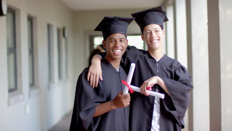 Two-teenage-biracial-boys-in-graduation-caps-and-gowns-smile-broadly