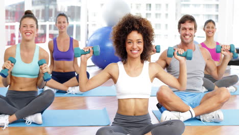 Fitness-class-sitting-in-lotus-pose-together-lifting-dumbbells