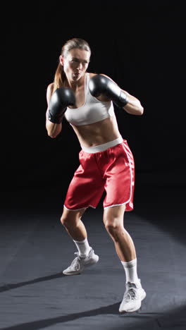 Vertical-video:-Caucasian-female-boxer-wearing-boxing-gloves,-black-background