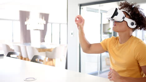 A-young-biracial-man-with-curly-hair-wears-yellow-shirt-in-kitchen,-copy-space