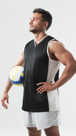 Vertical-video:-Biracial-male-athlete-holding-volleyball,-white-background