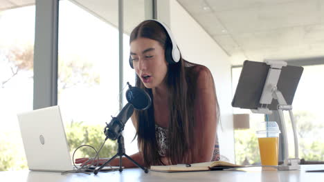 Teenage-Caucasian-girl-with-microphone-and-headphones-focuses-on-her-laptop