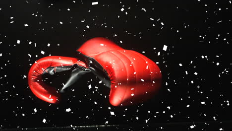 Animation-of-white-confetti-falling-over-red-boxing-gloves-on-black-background