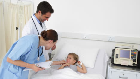 Sick-little-girl-lying-in-bed-talking-to-nurse-and-doctor