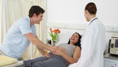 Brunette-pregnant-woman-lying-on-bed-talking-with-partner-and-doctor