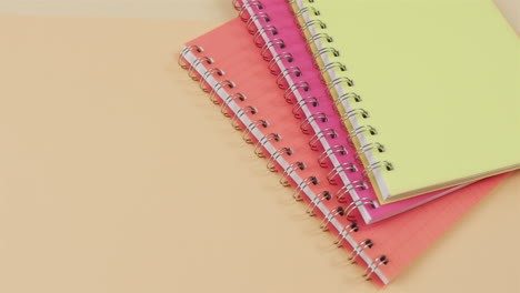 Colorful-spiral-notebooks-are-stacked-on-a-dual-toned-pink-and-yellow-background,-with-copy-space