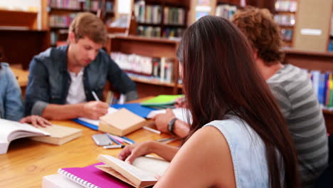 Estudiantes-Trabajando-Juntos-En-La-Biblioteca-Con-Una-Chica-Sonriendo-A-La-Cámara