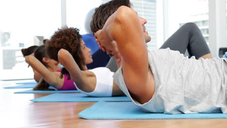 Fitness-class-sitting-up-together-on-exercise-mats