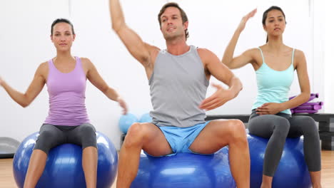 Fitness-class-sitting-on-exercise-balls-stretching-