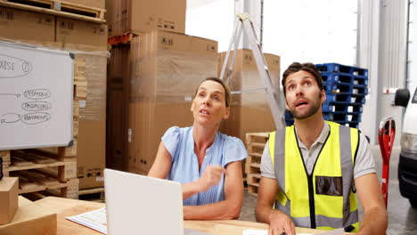 Warehouse-workers-using-laptop-and-pointing-shelves