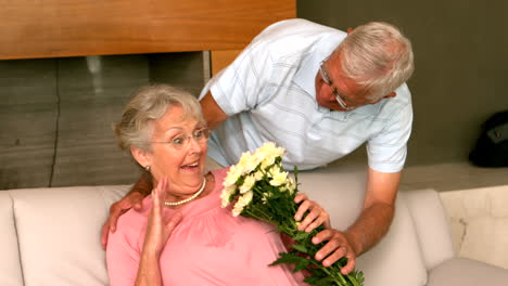 Un-Hombre-Mayor-Sorprende-A-Su-Pareja-Con-Flores-En-El-Sofá