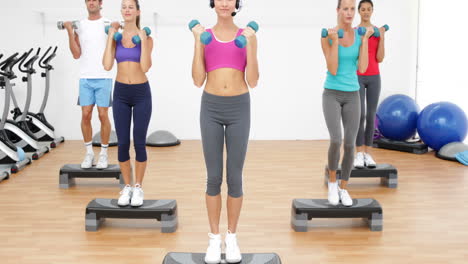 Aerobics-class-stepping-together-led-by-instructor-and-lifting-dumbbells