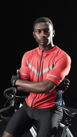 Vertical-video:-African-American-male-athlete-posing-with-bike,-black-background