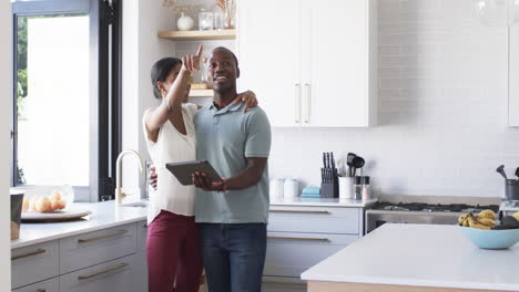 A-diverse-couple-using-tablet-and-pointing-in-the-kitchen-with-copy-space