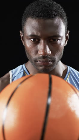 Vertical-video:-African-American-male-athlete-holding-basketball,-black-background