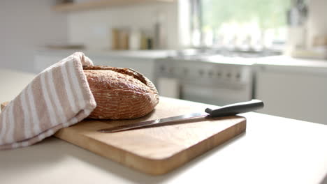 Fresh-bread-resting-on-wooden-cutting-board,-covered-with-a-cloth