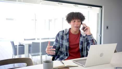 A-young-biracial-man-is-on-a-phone-call,-using-a-laptop-with-copy-space