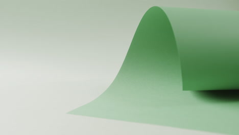 Nahaufnahme-Eines-Grünen,-Aufgerollten-Stück-Papier-Auf-Weißem-Hintergrund-Mit-Kopierraum-In-Zeitlupe