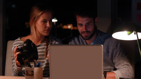 Casual-colleagues-using-laptop-and-camera-at-night