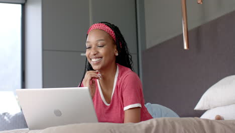 African-American-young-woman-lying-on-bed,-using-laptop