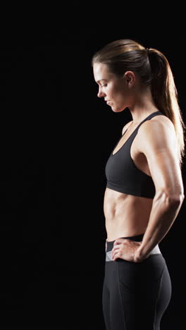 Vertical-video:-Caucasian-female-athlete-standing,-black-background