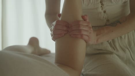 Woman-massaging-a-leg-in-a-bright,-serene-room,-close-up