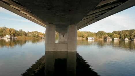 Drone-captures-a-tranquil-European-river,-revealing-the-underside-of-a-bridge