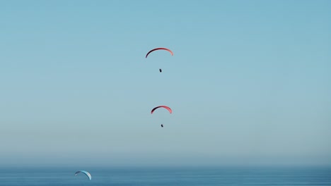 Paragliders-flying-in-blue-skies-over-the-ocean,-sunny-morning