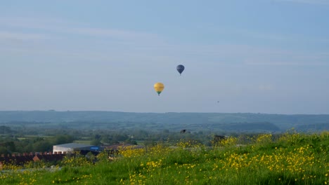 Malerische-Landschaftsansicht-Der-Ländlichen-Gegend-Mit-Gelben-Blumen-Und-Zwei-Heißluftballons,-Die-über-Die-Ebenen-Von-Somerset-Fliegen