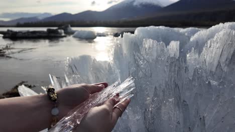 Una-Persona-Se-Encuentra-Junto-A-Una-Masa-De-Agua,-Sosteniendo-Un-Trozo-De-Hielo