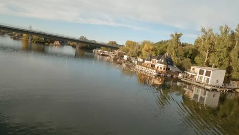 Drone-footage-of-colorful-houseboats-moored-on-a-calm-river-with-a-bridge-in-the-background
