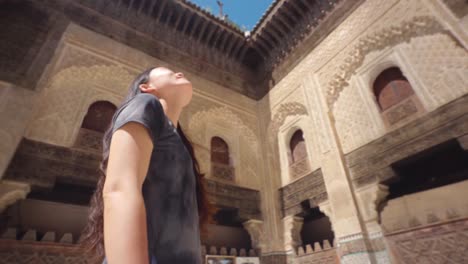 Orbita-Alrededor-De-Una-Mujer-Asiática-Mirando-Hacia-Arriba-Mientras-Explora-Con-Asombro-La-Belleza-De-La-Madraza-Bou-Inania-En-Fez,-Marruecos.