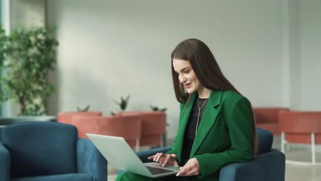 Charmante-Frau-Lacht,-Während-Sie-Mit-Einem-Laptop-In-Der-Lobby-Eines-Business-Centers-Sitzt