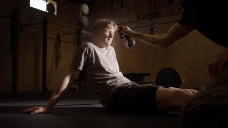 Sitzender-Männlicher-Fitnessstudio-Enthusiast-Wird-Zur-Abkühlung-Mit-Einer-Wasserflasche-Besprüht