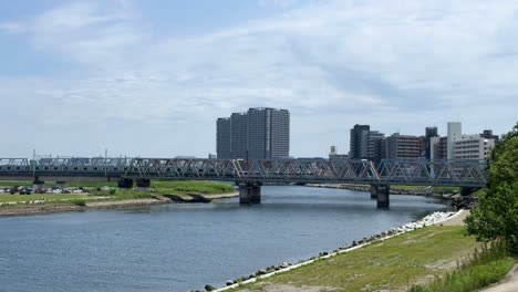 Ein-Stadtfluss-Mit-Einer-Brücke-Und-Modernen-Gebäuden-Unter-Einem-Teilweise-Bewölkten-Himmel