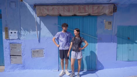 White-male-and-asian-woman-playfully-pose-against-blue-colorful-building-wall-in-Morocco
