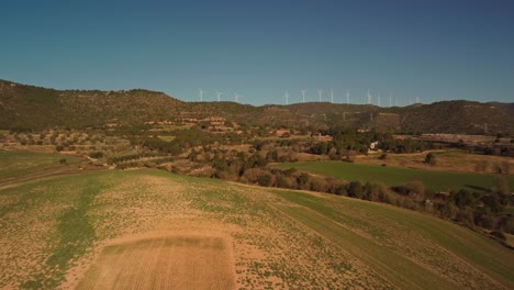 Windmills-spinning-in-the-distance-over-green-and-brown-fields-near-Igualada,-Barcelona