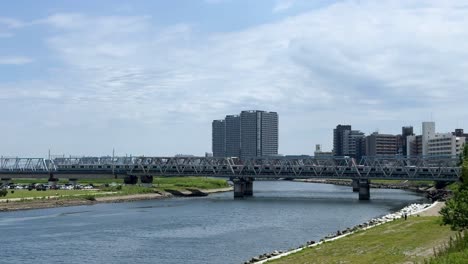 A-scenic-view-of-a-river-with-a-bridge-and-city-buildings-under-a-clear-blue-sky