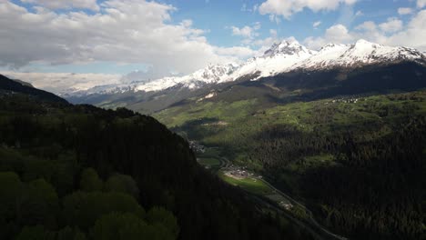 Aerial-view-of-the-valley-in-Obersaxen,-Graubünden,-Switzerland,-encircled-by-snow-covered-mountain-peaks