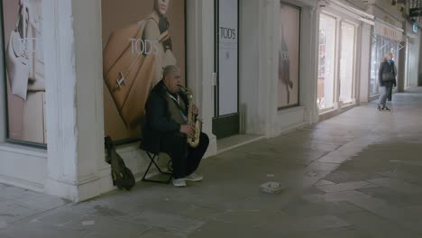 Street-musician-playing-saxophone-outside-luxury-store-in-Venice-at-night