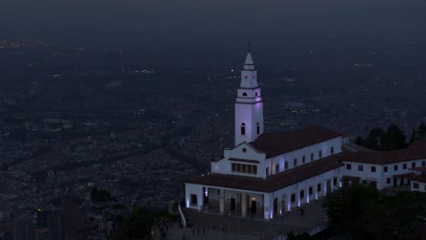 Drone-shot-of-Monserrate-church-overlooking-the-city-of-Bogota,-Colombia-at-blue-hour