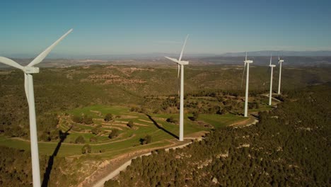 Molinos-De-Viento-En-Igualada,-Barcelona-En-Un-Día-Soleado-Con-Colinas-Verdes-Y-Cielos-Despejados,-Vista-Aérea