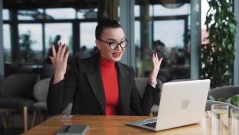 Una-Joven-Severa-Vestida-De-Negocios-Discute-Y-Hace-Gestos-Con-Las-Manos-Durante-Una-Videollamada-En-Una-Computadora-Portátil,-Sentada-En-Una-Oficina