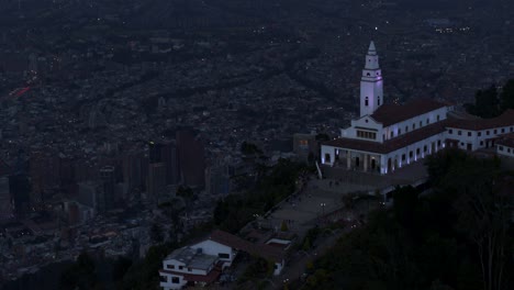 Drone-shot-of-Monserrate-church-overlooking-the-city-of-Bogota,-Colombia-at-blue-hour