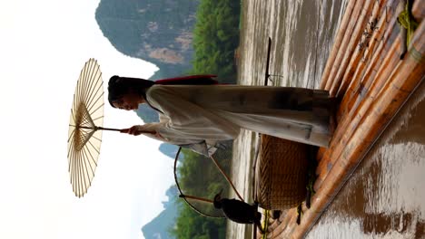 Niña-Hanfu-Hace-Girar-Un-Paraguas-Tradicional-En-Una-Balsa-De-Bambú,-Xingping,-China